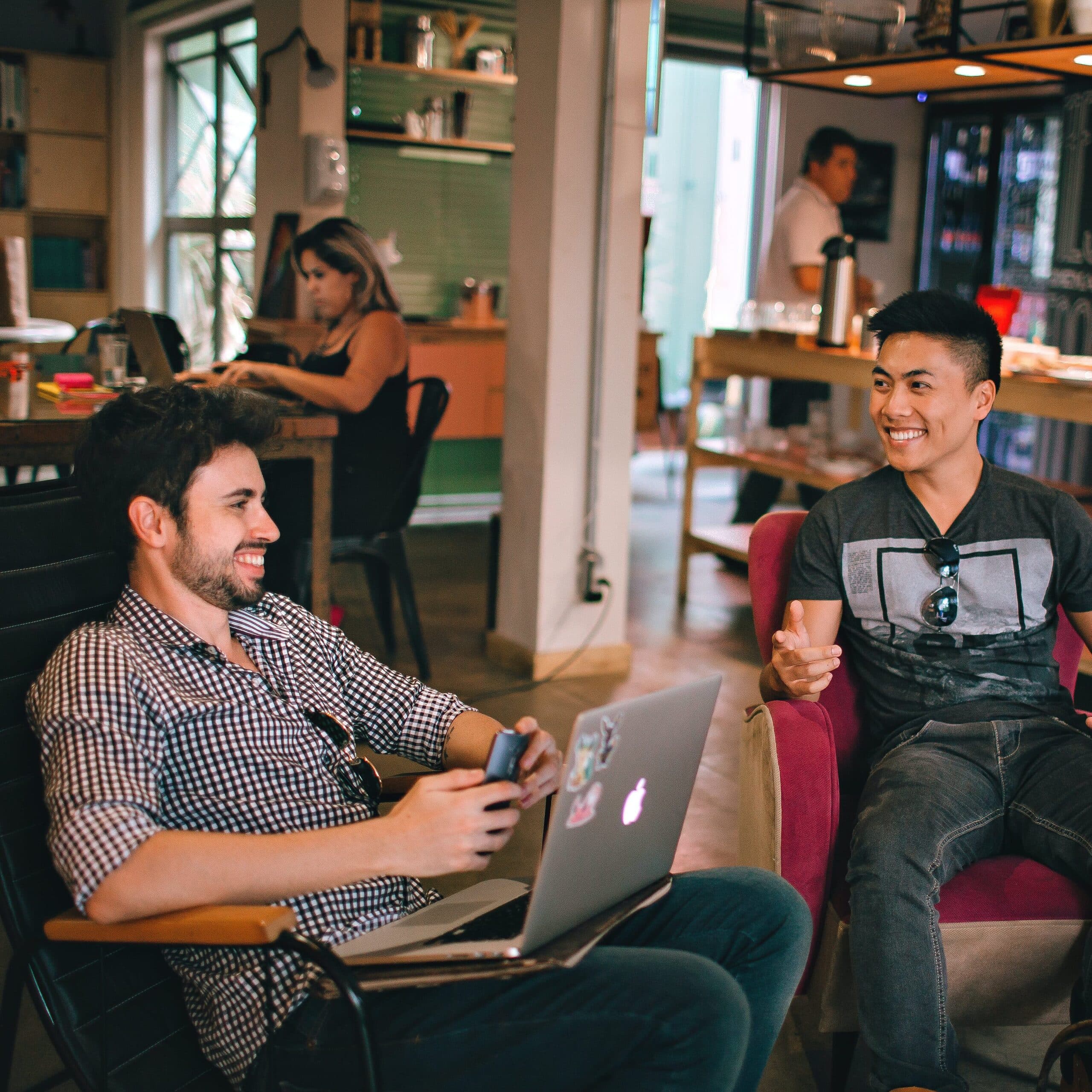 Two men talking and laughing in a café, one with a laptop
