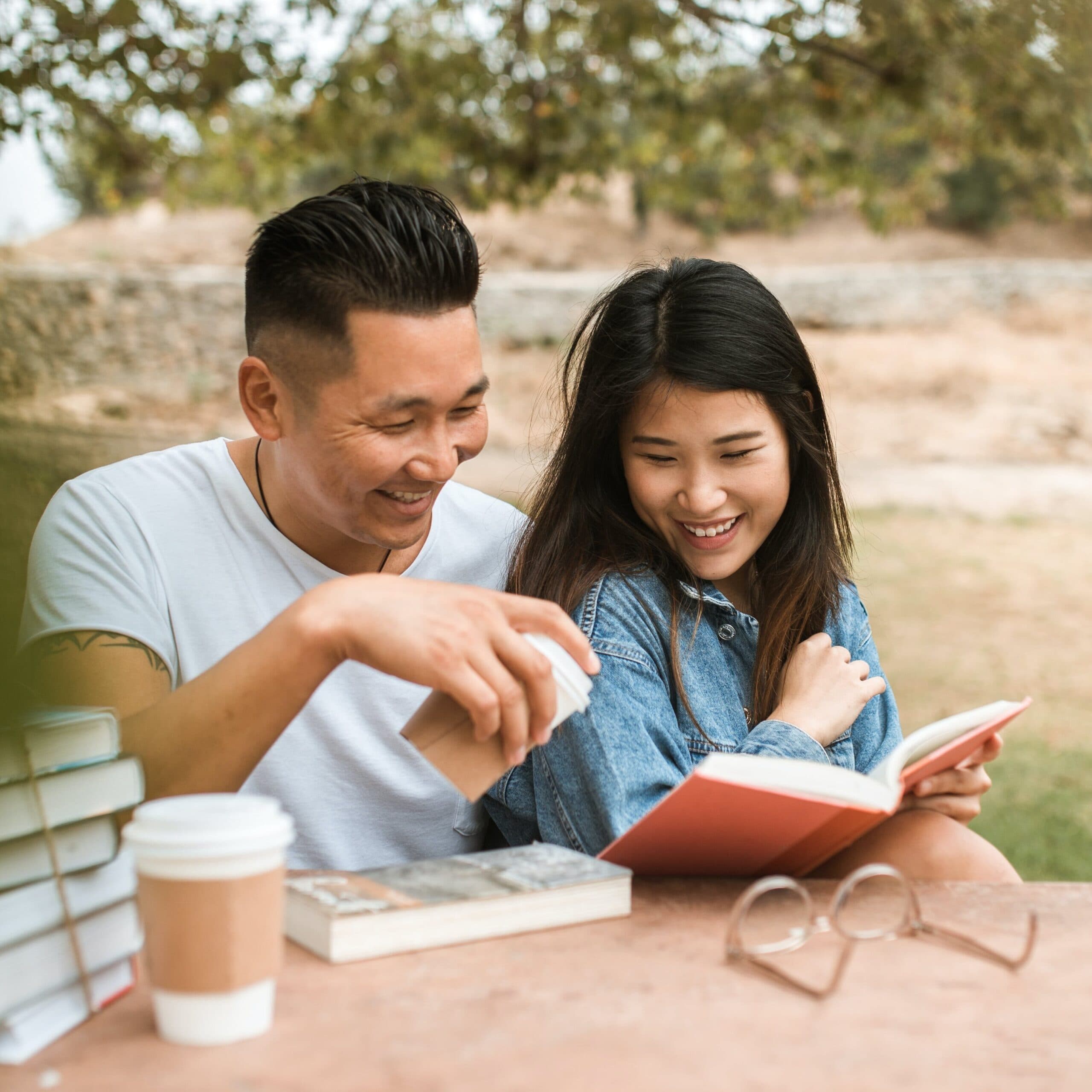 Two adults laughing together over an open book at an outdoor table